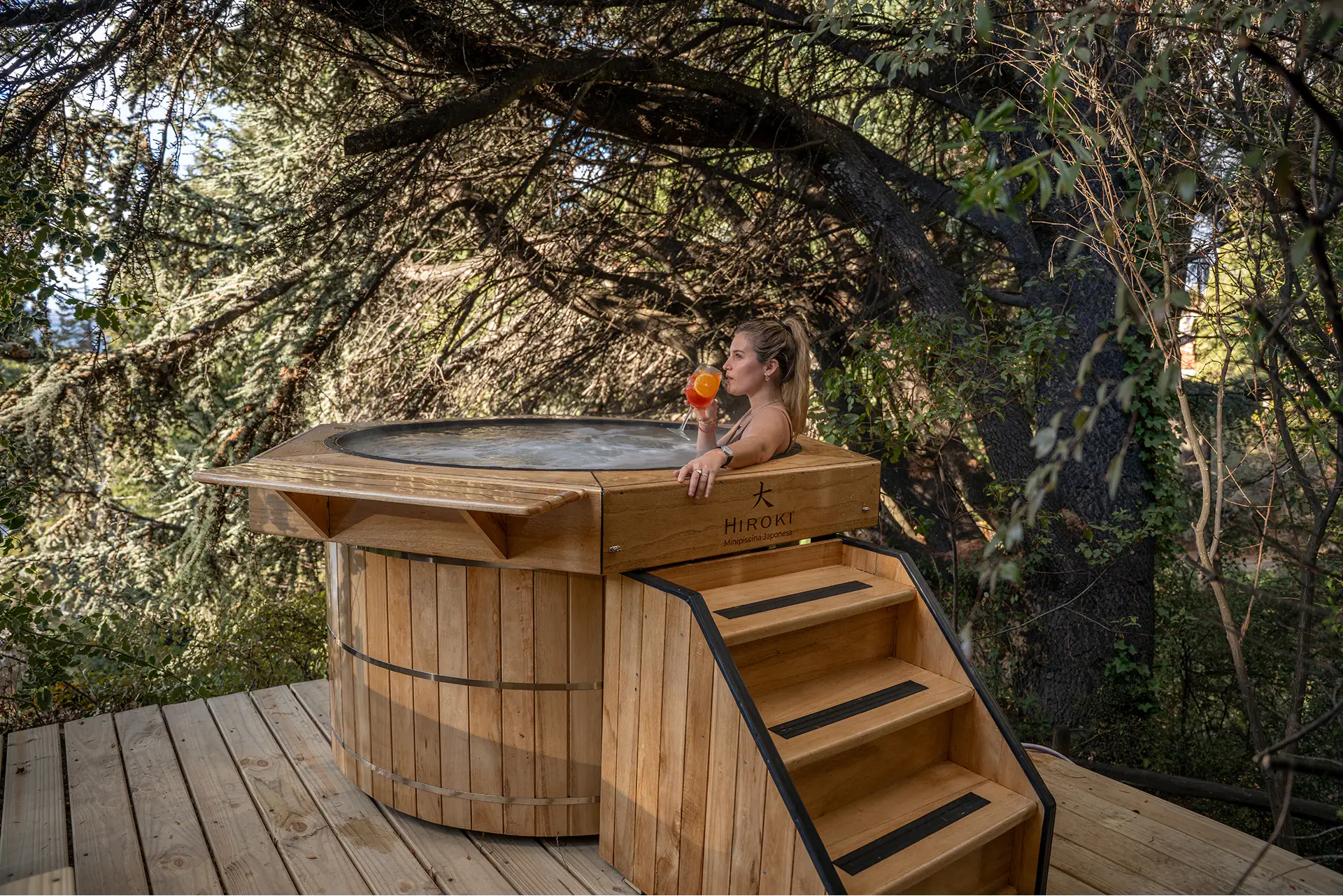 Persona en una minipiscina Hiroki de madera sobre un deck rodeado de árboles en La Cascada Casa Patagónica.
